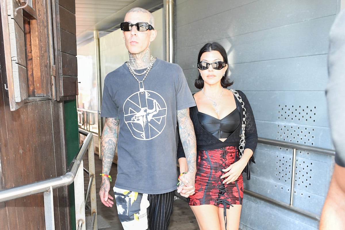 Travis Barker and Kourtney Kardashian wear sunglasses and hold hands while walking.