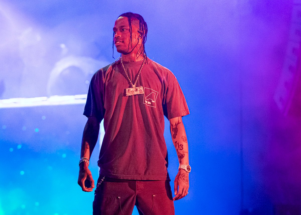 Travis Scott stands on stage, illuminated by blue and purple lights behind him.