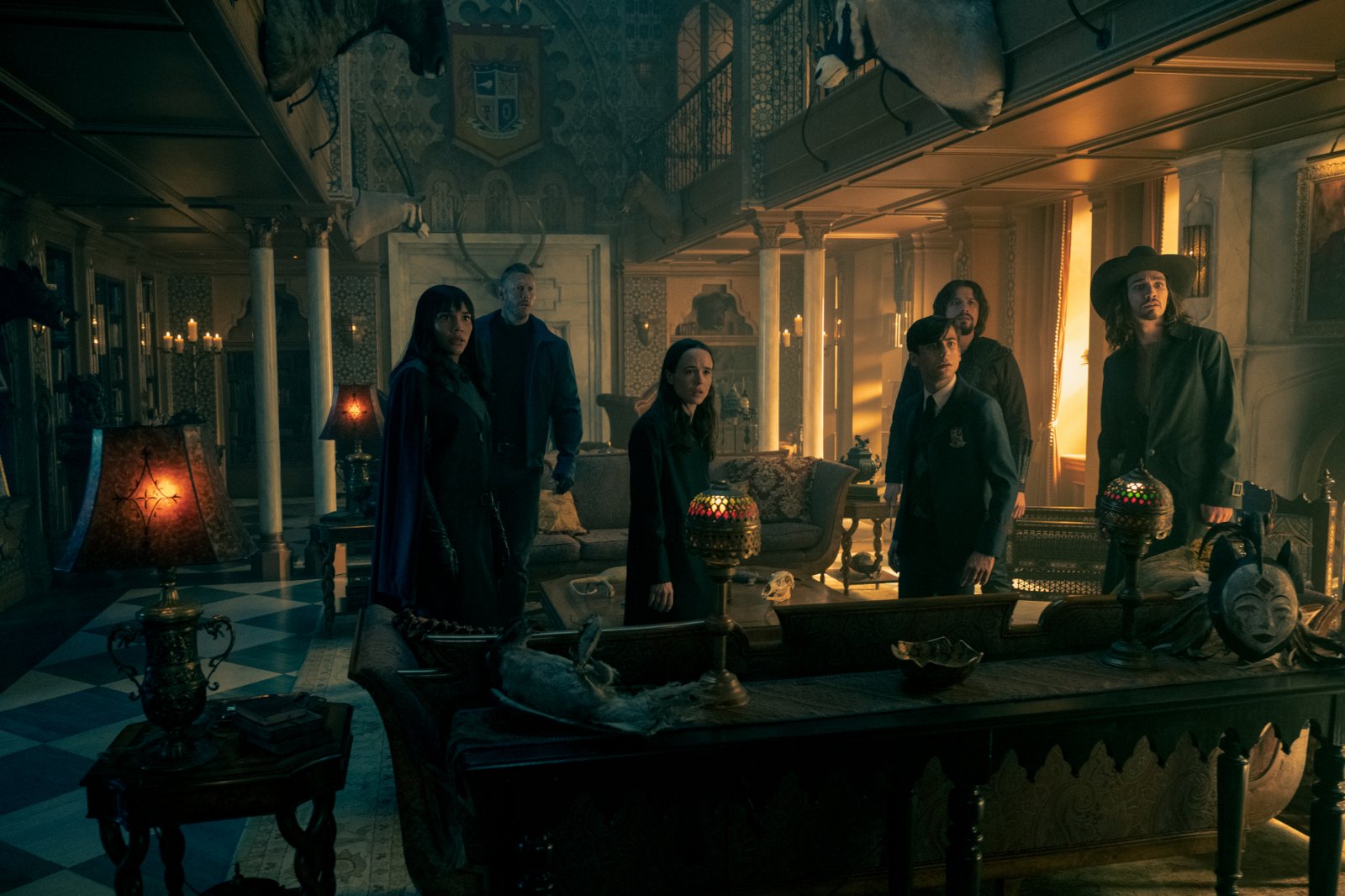 Emmy Raver-Lampman, Tom Hopper, Elliot Page, Aidan Gallagher, David Castañeda, and Robert Sheehan in 'The Umbrella Academy' Season 2 Episode 10. They're standing in the Hargreeves family's living room and looking up at something.
