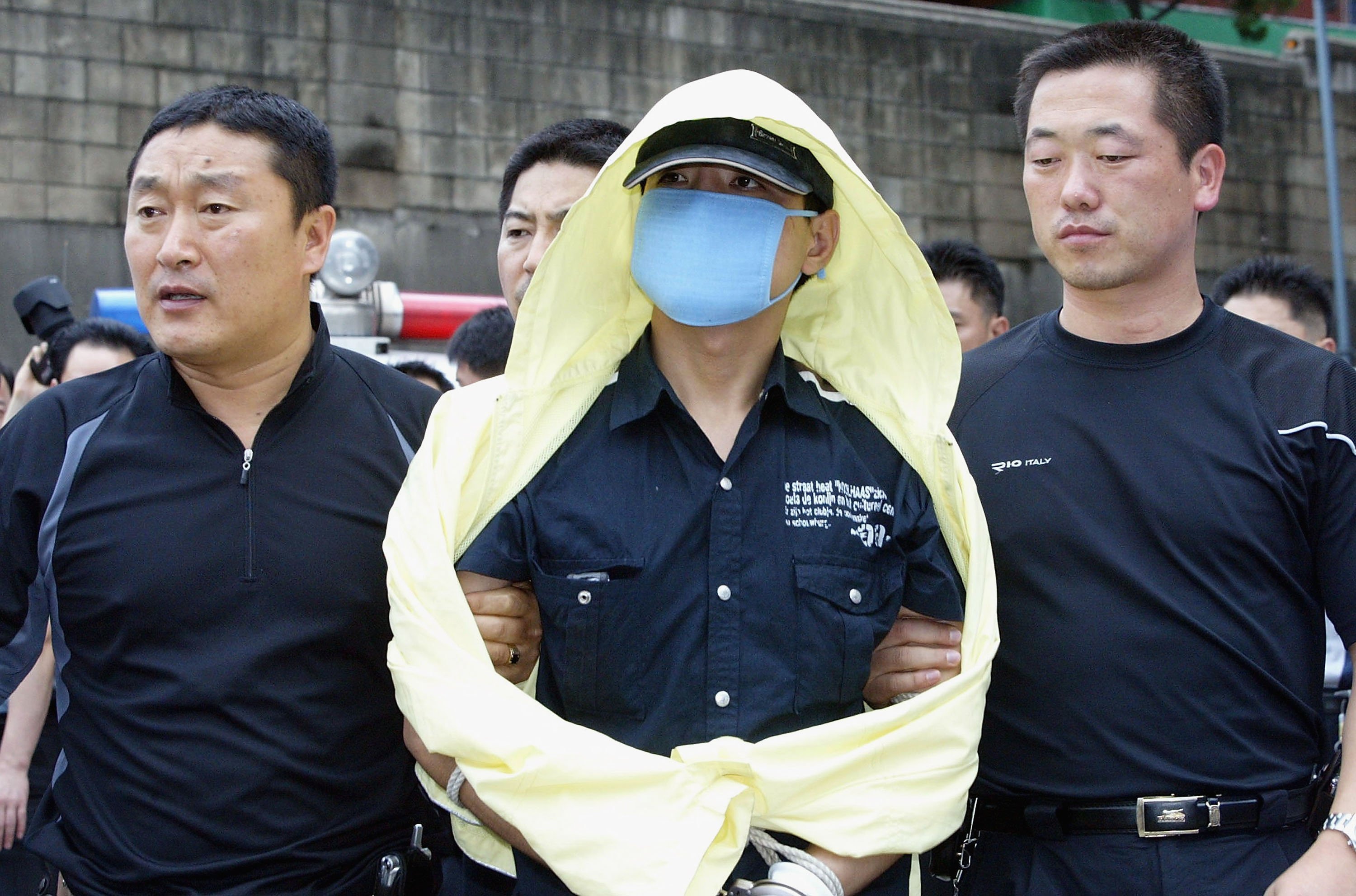 Serial killer Yoo Young-Chul ‘The Raincoat Killer: Chasing a Predator in Korea’ wearing medical mask, yellow crime coat being escorted to burial sites