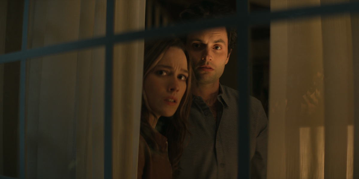 Joe Goldberg and Love Quinn stare with worried expressions out the window in 'You' Season 3.