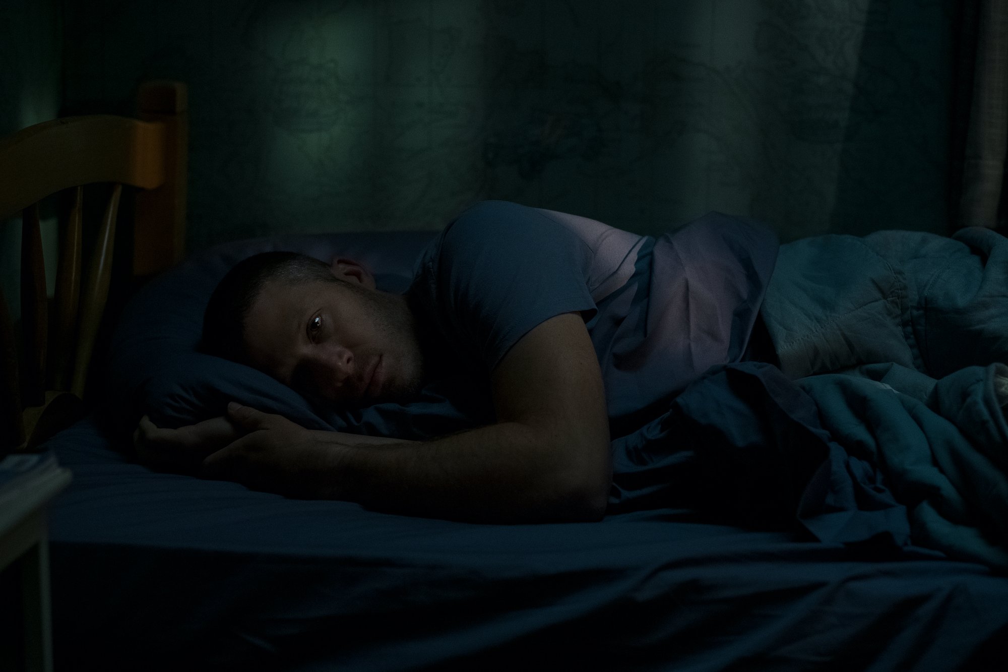 Zach GIlford as Riley Flynn, seen laying in bed in the Netflix series 'Midnight Mass'