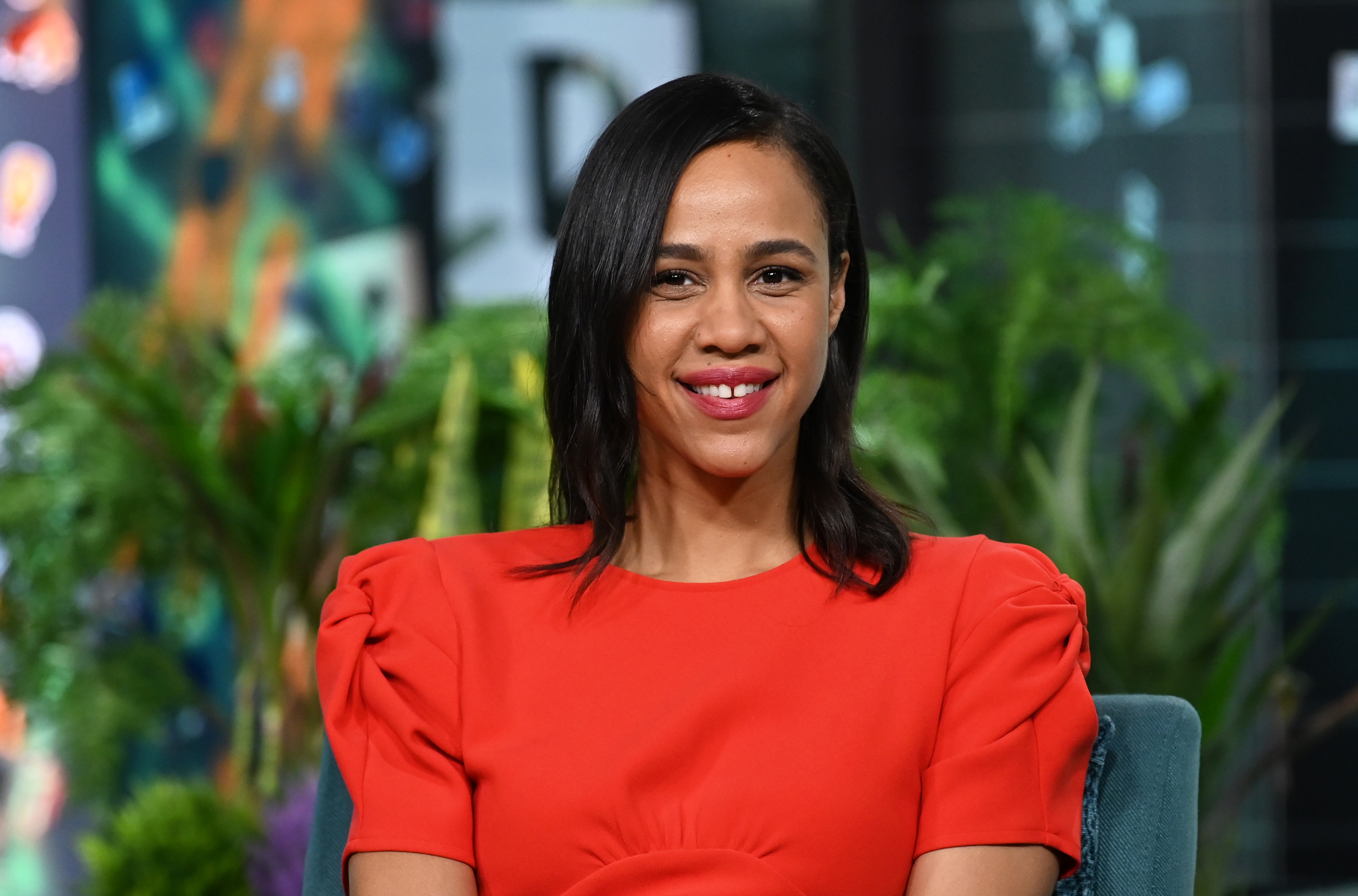 Zawe Ashton smiles while wearing a red dress during an appearance on the Build SeriesA=
