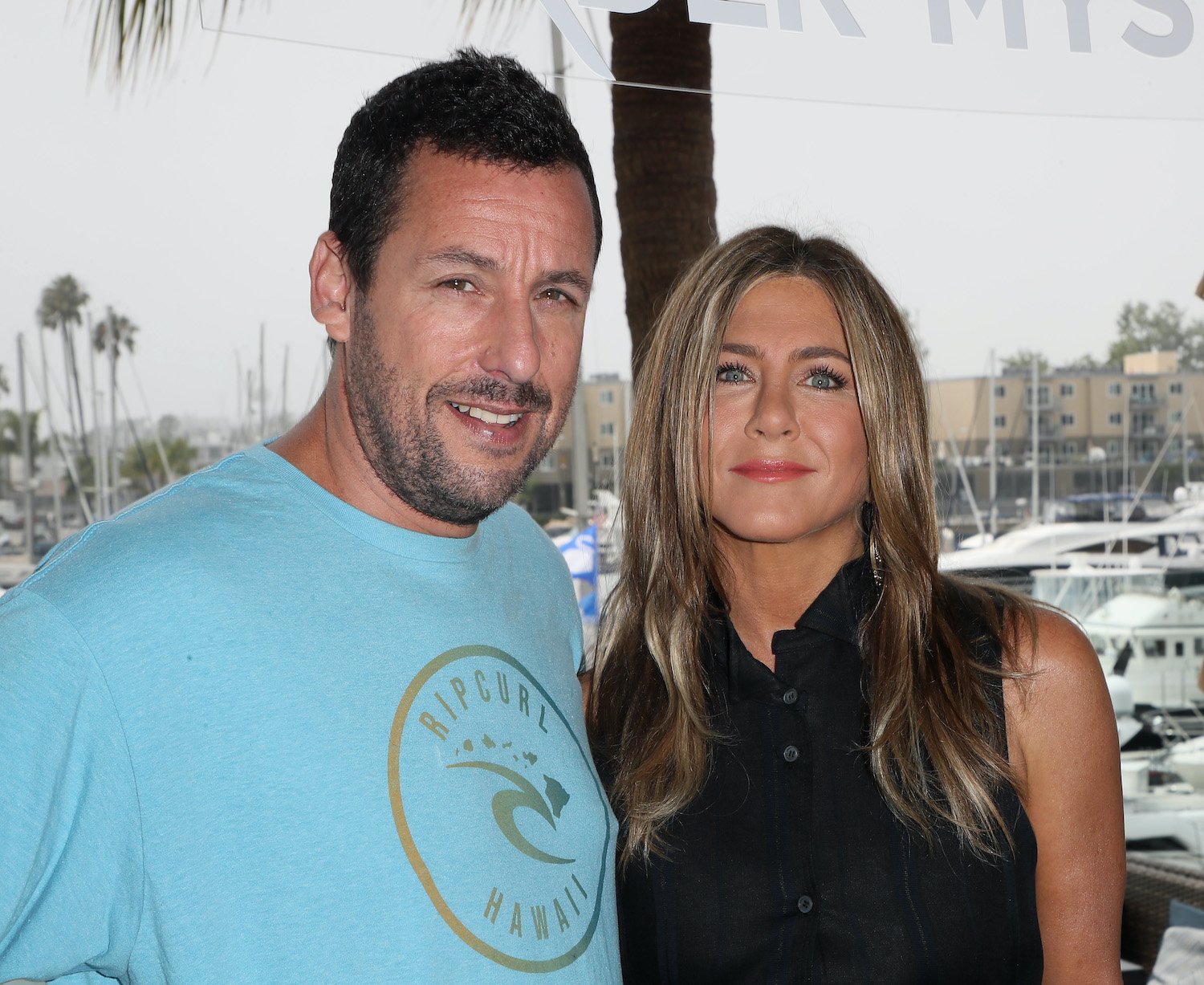 Adam Sandler wears a blue shirt and Jennifer Aniston wears a black shirt as they smile during a photocall of Netflix's 'Murder Mystery' in 2019