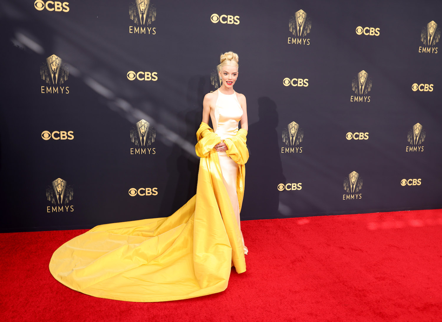 Anya Taylor-Joy wears a pale yellow Dior gown and vibrant yellow opera coat on the 2021 Emmys red carpet