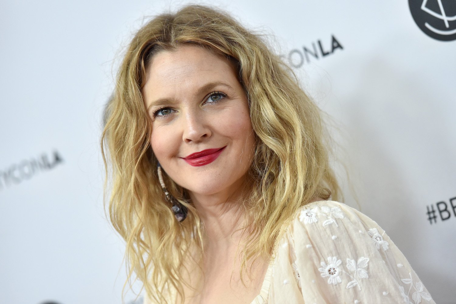 Drew Barrymore wears a white top and red lip as she smiles on the red carpet at Beautycon Festival LA 2018