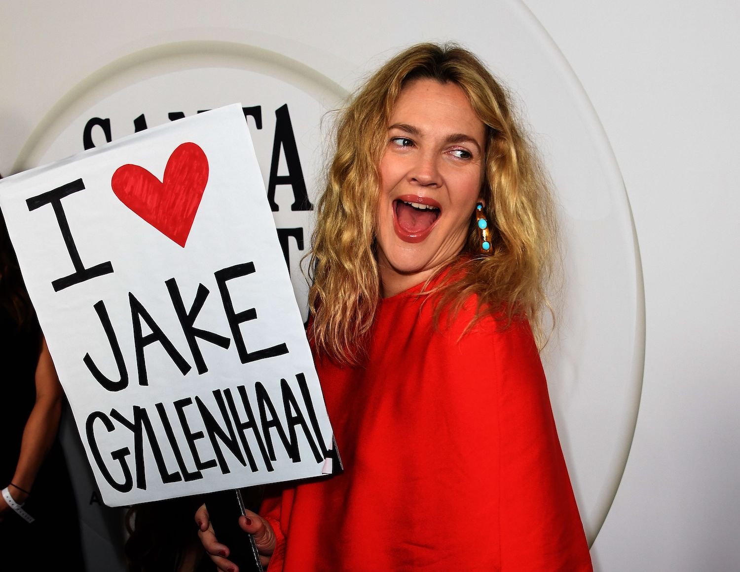 Drew Barrymore wears red and holds a sign that says I Love Jake Gyllenhaal at the season 2 premier for 'Santa Clarita Diet'