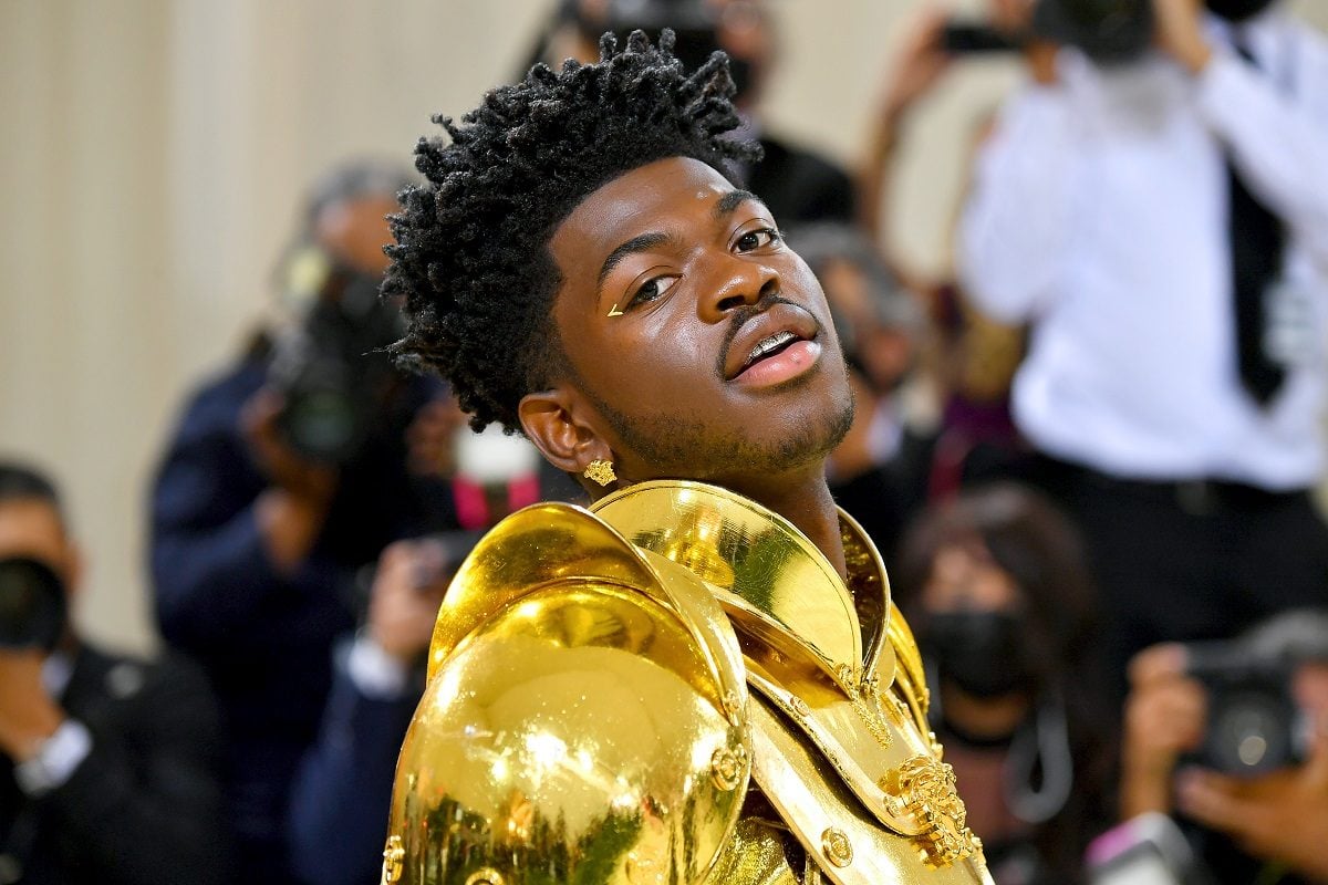 Lil Nas X poses while wearing a gold outfit.