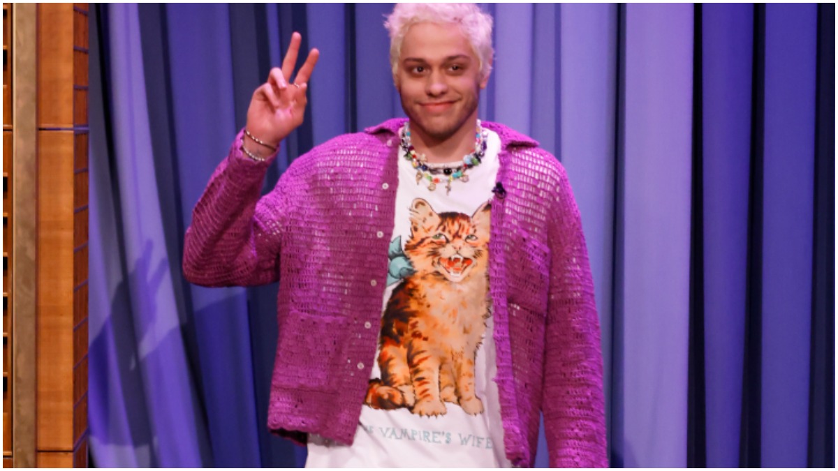 Pete Davidson wears a lavender jacket and a graphic t-shirt.