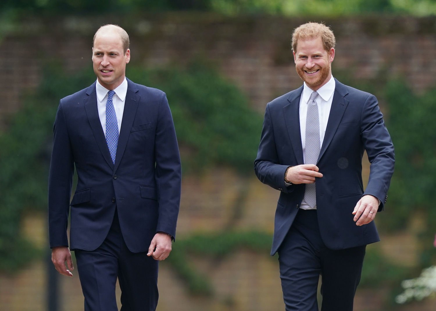 Prince William and Prince Harry wear suits as they walk and talk during their arrival for the unveiling of a Princess Diana statue in the Sunken Garden at Kensington Palace