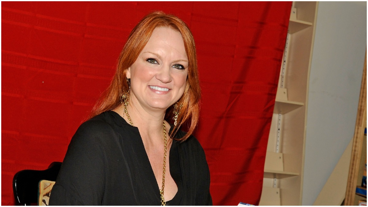 Ree Drummond smiles wearing a black shirt in front of a red background