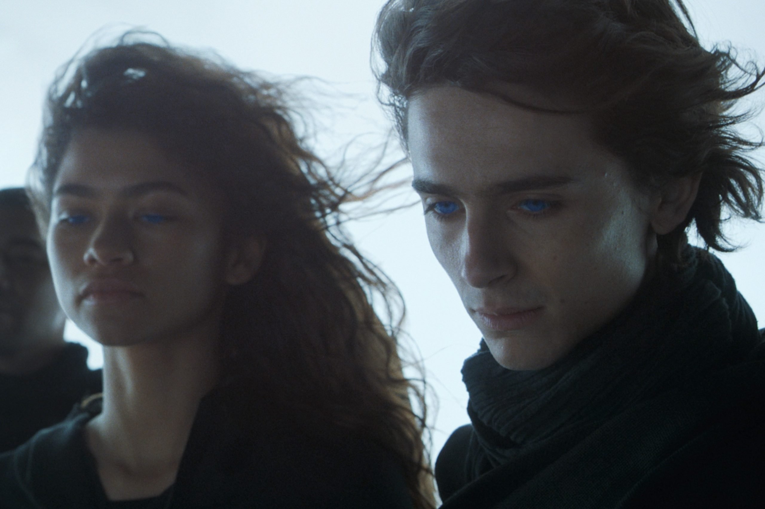 Zendaya and Timothée Chalamet , in black costumes, looking down to something in a still from the movie 'Dune.'