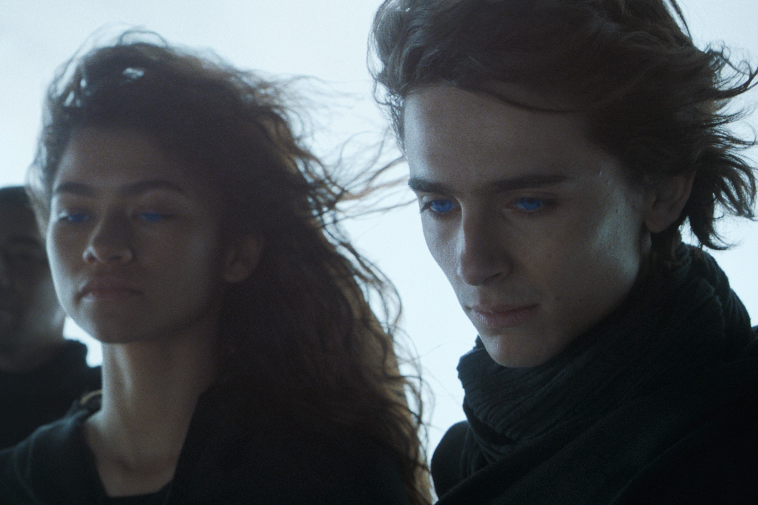 Zendaya and Timothée Chalamet , in black costumes, looking down to something in a still from the movie 'Dune.'