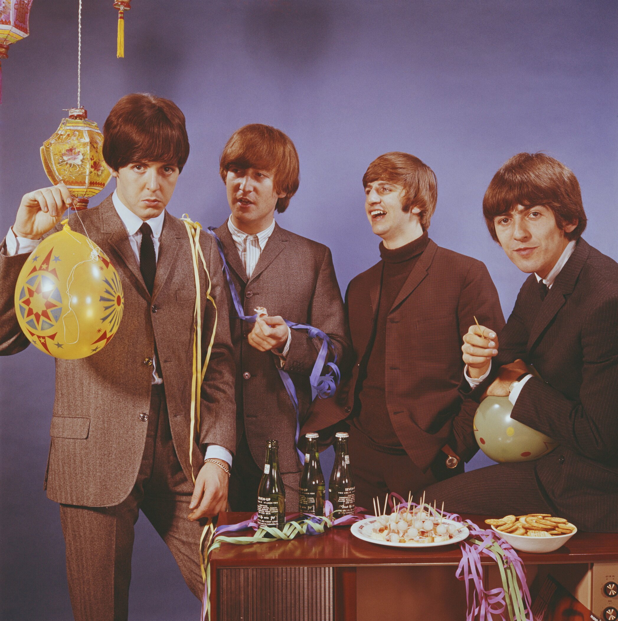 The Beatles pose with bottles of beer, party snacks, and balloons in October 1964. Left to right: Paul McCartney, John Lennon (1940-1980), Ringo Starr, and George Harrison (1943-2001). The session was taken to promote the BBC World Service.
