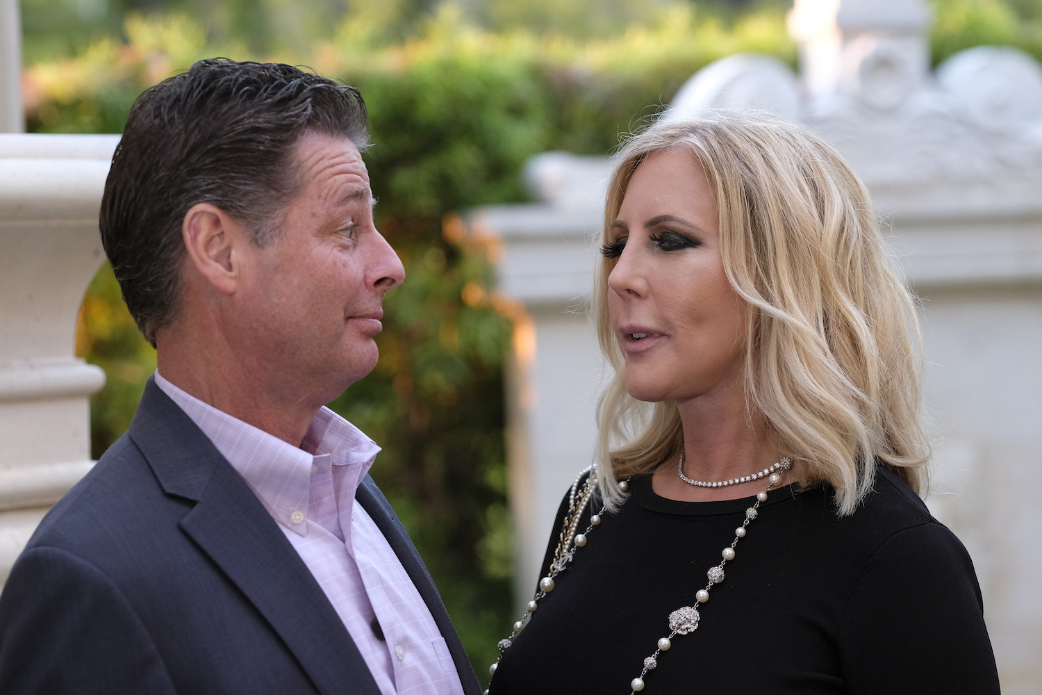 Steve Lodge wearing a suit looking at Vicki Gunvalson, wearing a black top and necklace.