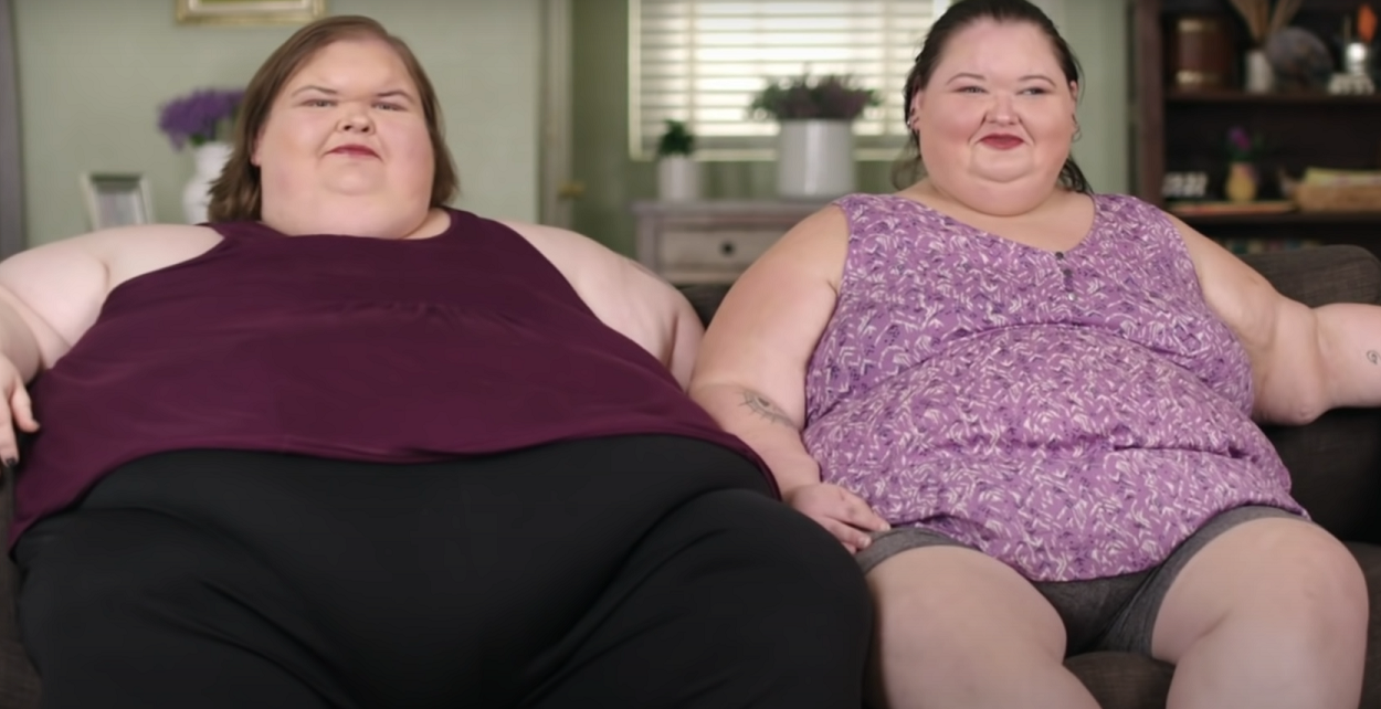 1000-Lb Sisters Season 3 stars Tammy Slaton and Amy Slaton -- Tammy Slaton sits next to Amy Slaton on a couch, and the two look at the camera.