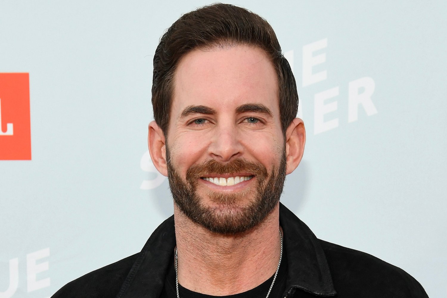 Tarek El Moussa smiles in front of a promotional backdrop