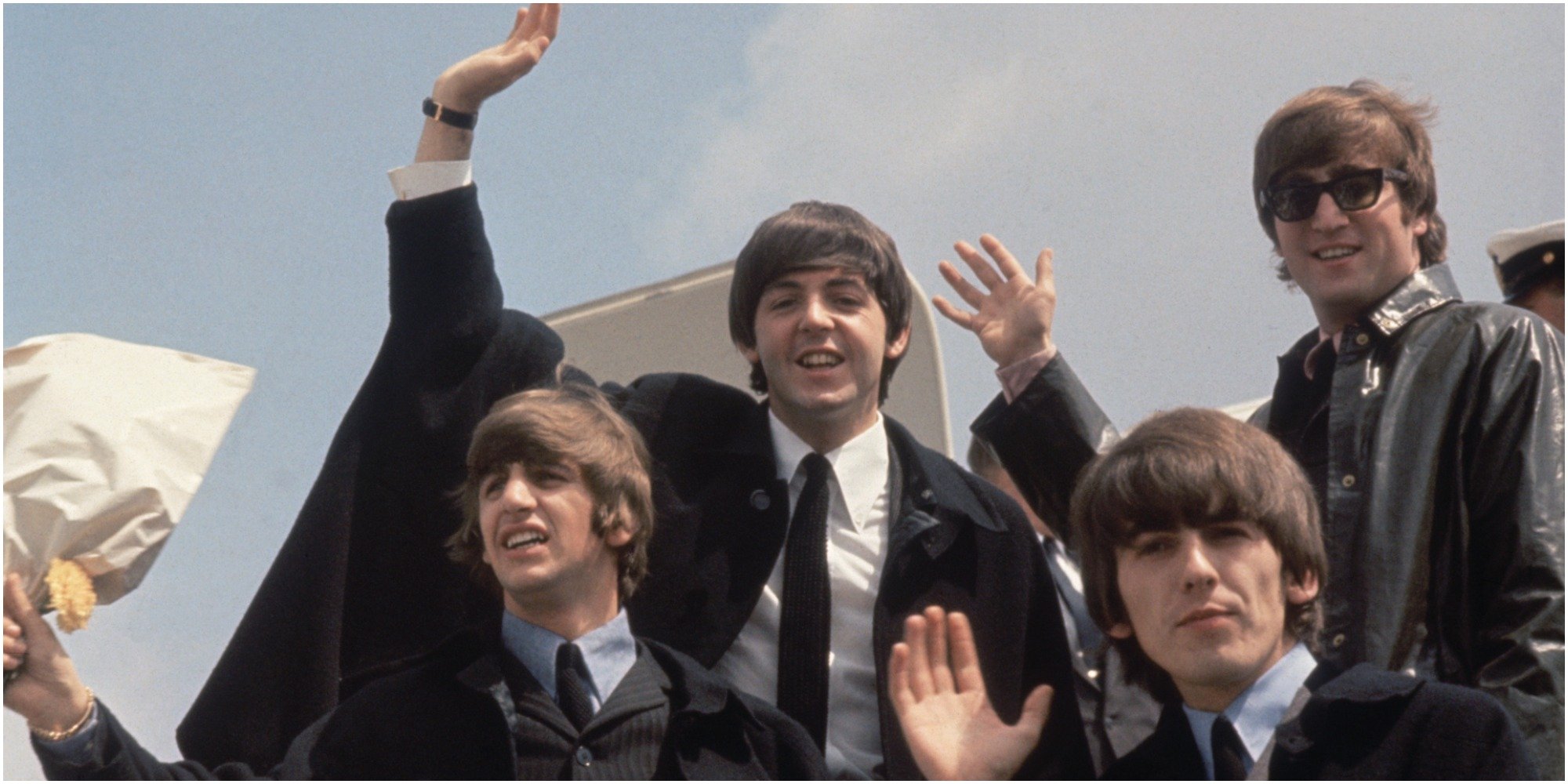 The Beatles wave from the steps of an airplane.