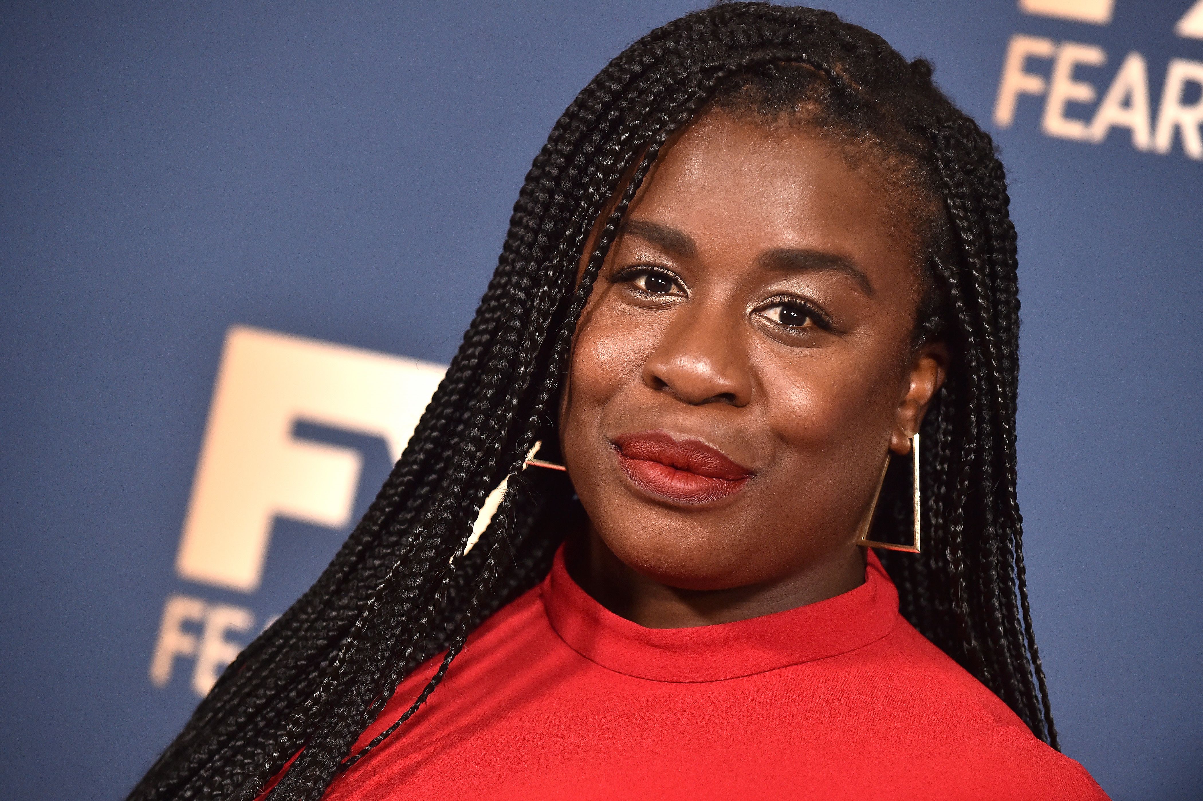 Uzo Aduba poses, tight smile, wearing a red dress