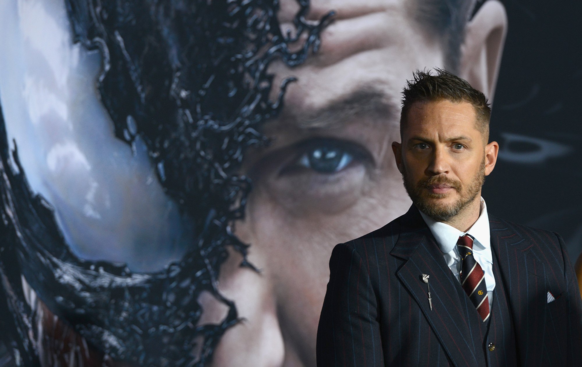 Tom Hardy stands in front of a 'Venom' poster at the 2018 premiere