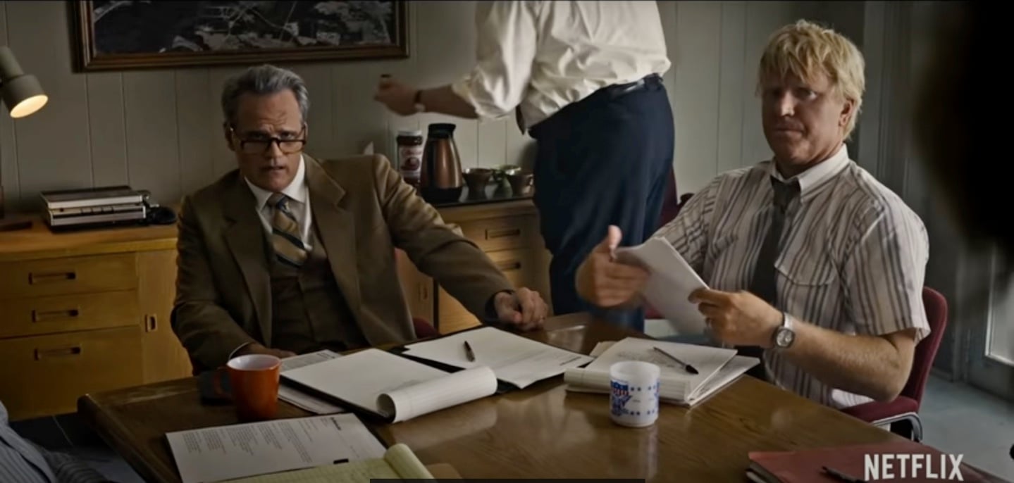 Michael Park as Tom Holloway and Jake Busey as Bruce Lowe sit at a table in a production still from 'Stranger Things' Season 2.