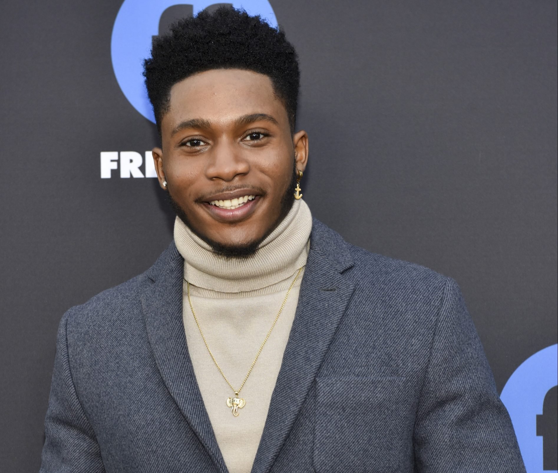 Actor Da'Vinchi wearing a gray suit jacket and a turtleneck to the 2018 Freeform Summit.
