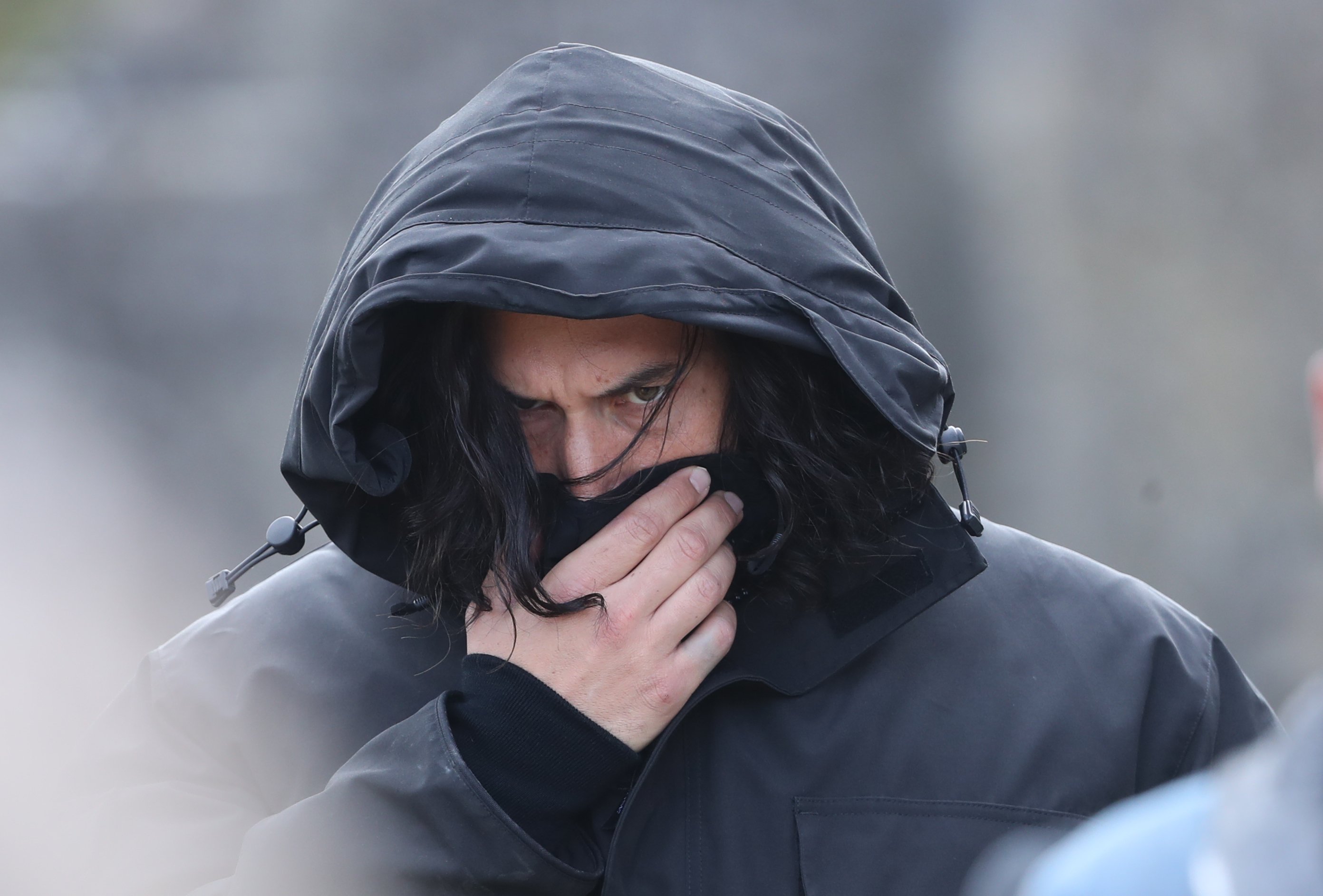 Adam Driver wearing a hooded jacket as he covers his face on the set of 'The Last Duel'