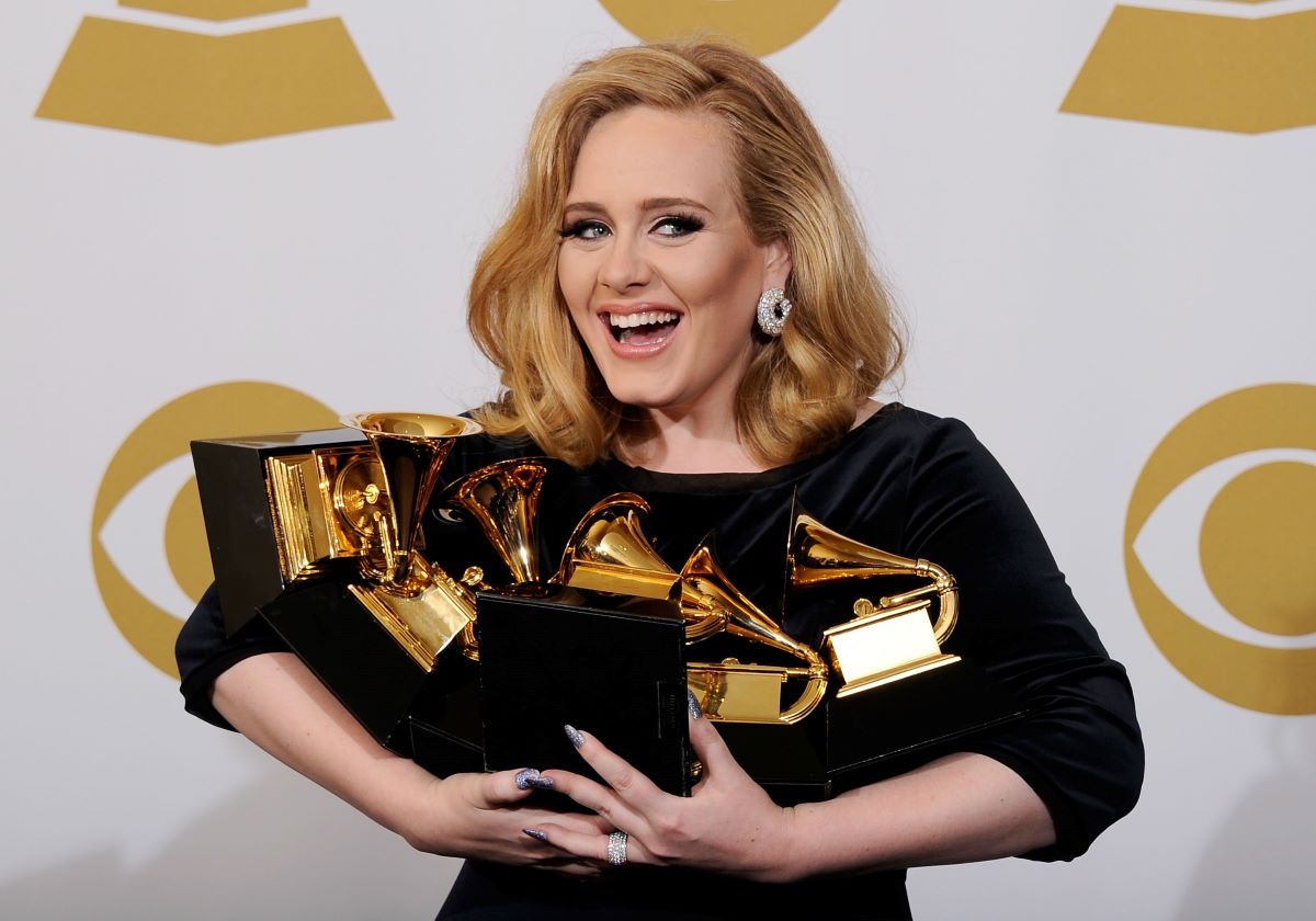 Adele smiling, holding an armful of Grammy awards
