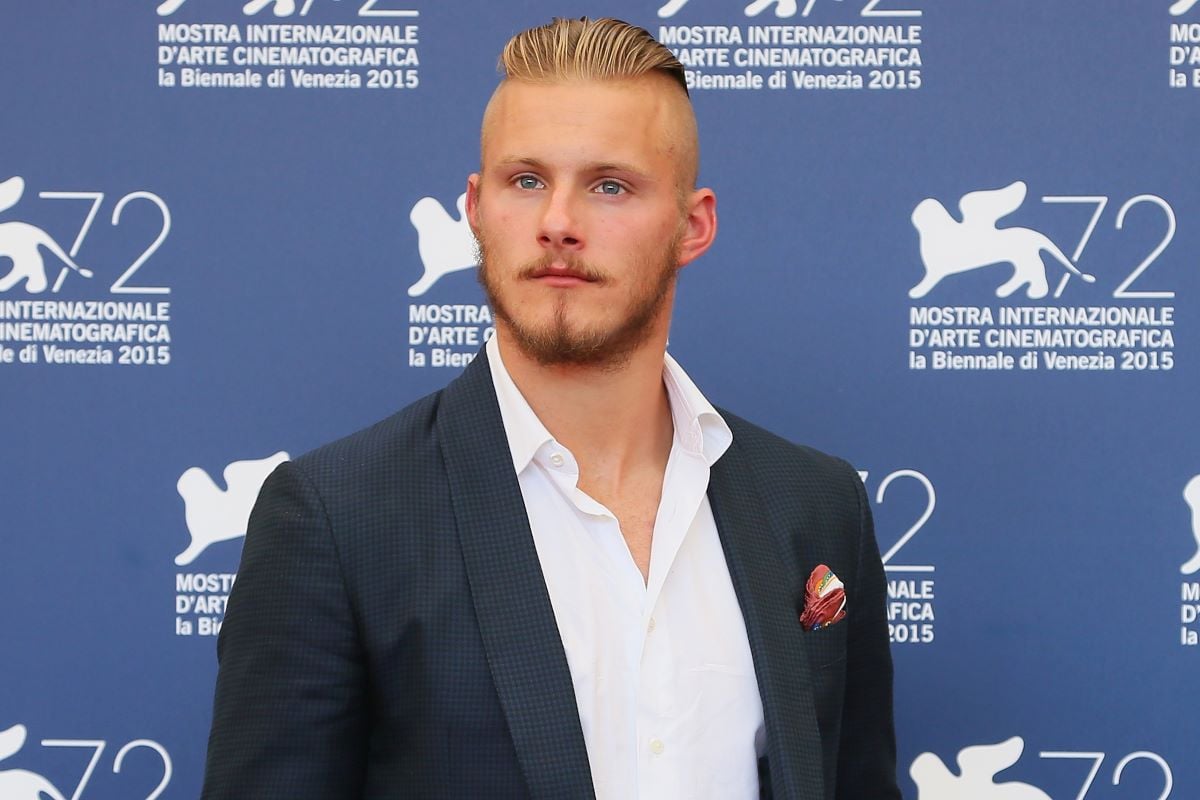Alexander Ludwig poses stoically in a dark suit 