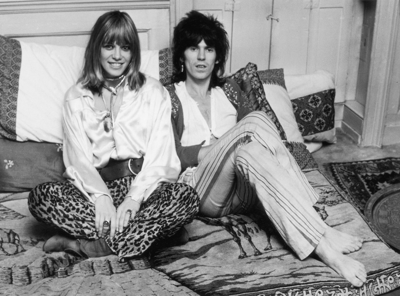 Anita Pallenberg and Keith Richards sit leaning against pillows.