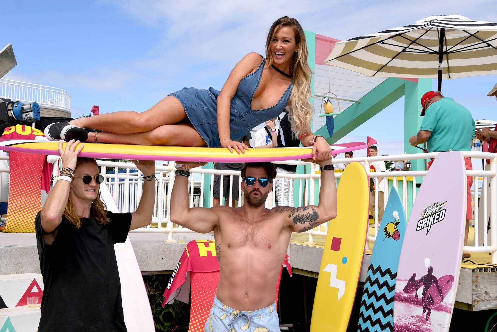 Ashley Mitchell lying on a surf board held up by Johnny 'Bananas' Devenanzio on the beach. MTV's 'The Challenge' Season 37 spoilers note Ashley Mitchell wins the elimination in episode 10.