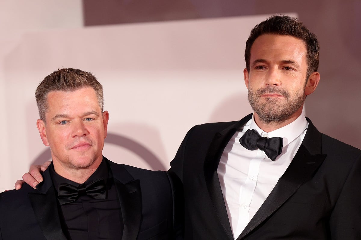 Matt Damon and Ben Affleck smiling at each other while wearing suits