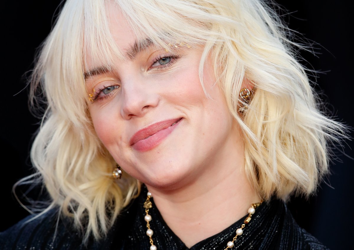 Billie Eilish smiles for the camera wearing gold makeup at an event.