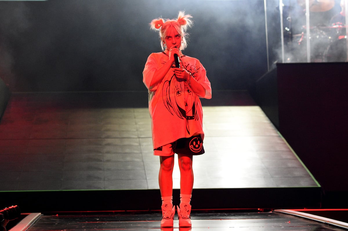 Billie Eilish performs on stage wearing pigtails, shorts, and an oversized T-shirt.