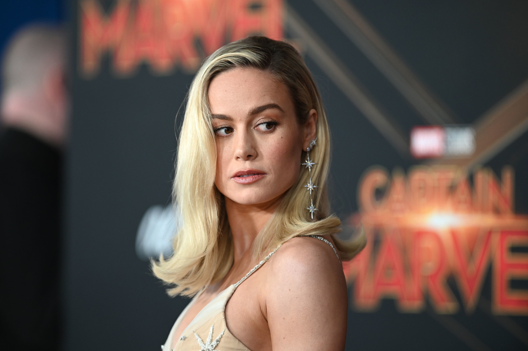 'Captain Marvel' star Brie Larson on the red carpet for the Marvel film. She's looking to the side, and her blonde hair is flipped up at the ends.