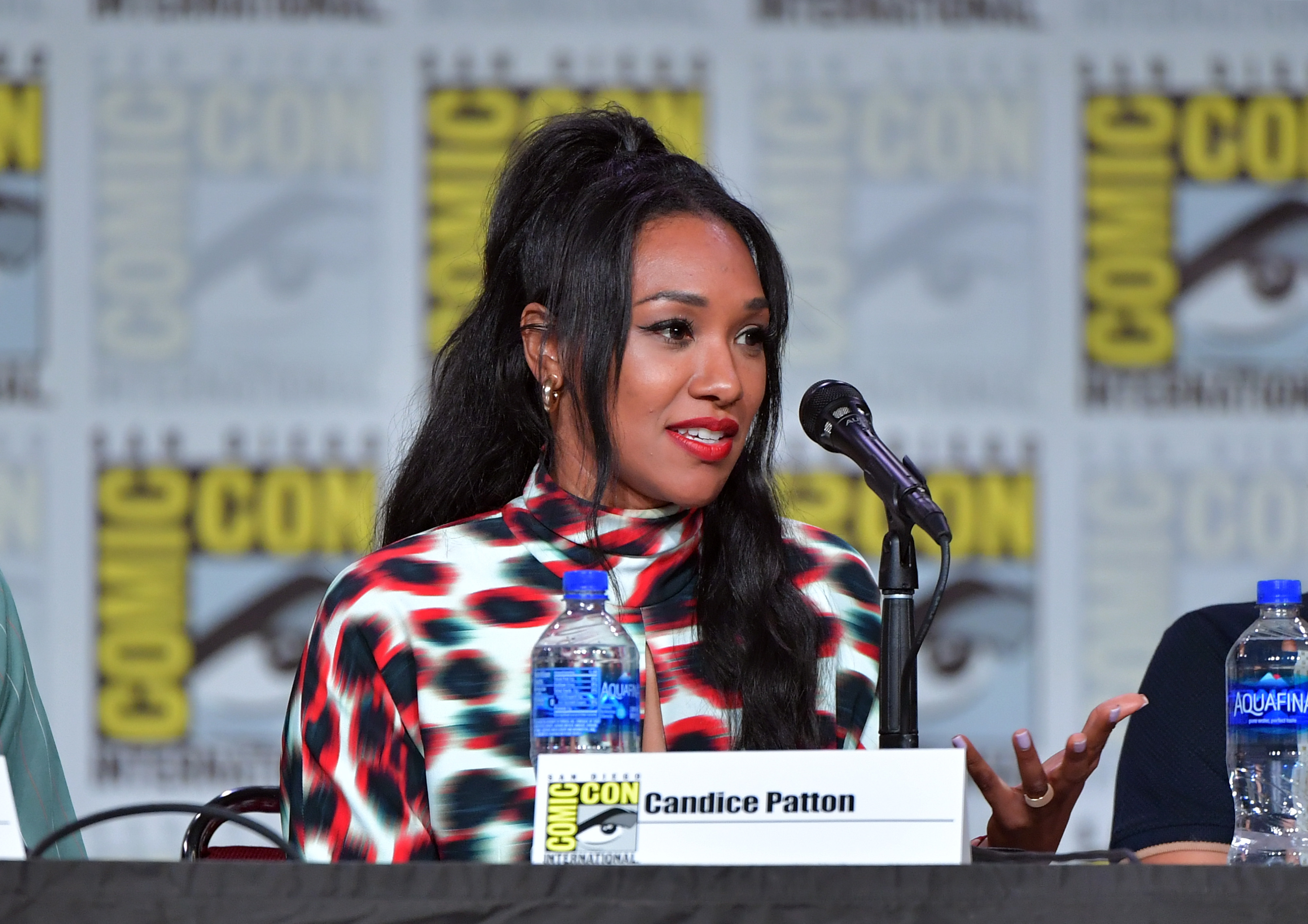 Candice Patton, who will be at DC FanDome 2021, wears a white long-sleeved, turtleneck dress with black and red smudged dots on it.