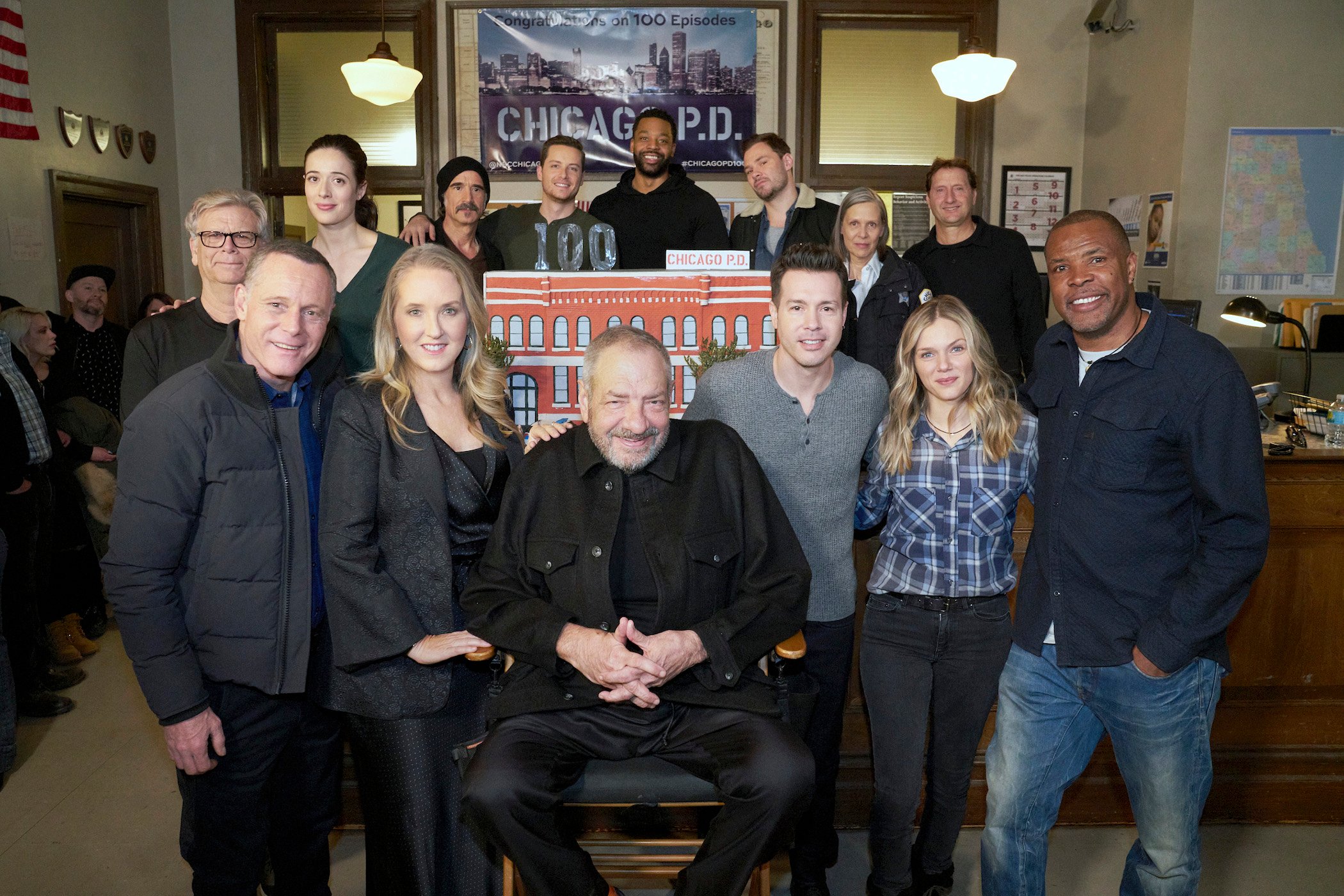 The 'Chicago P.D.' cast and Rick Eid standing and smiling to celebrate the 100th episode of the show. Many of these cast members are in 'Chicago P.D.' Season 9