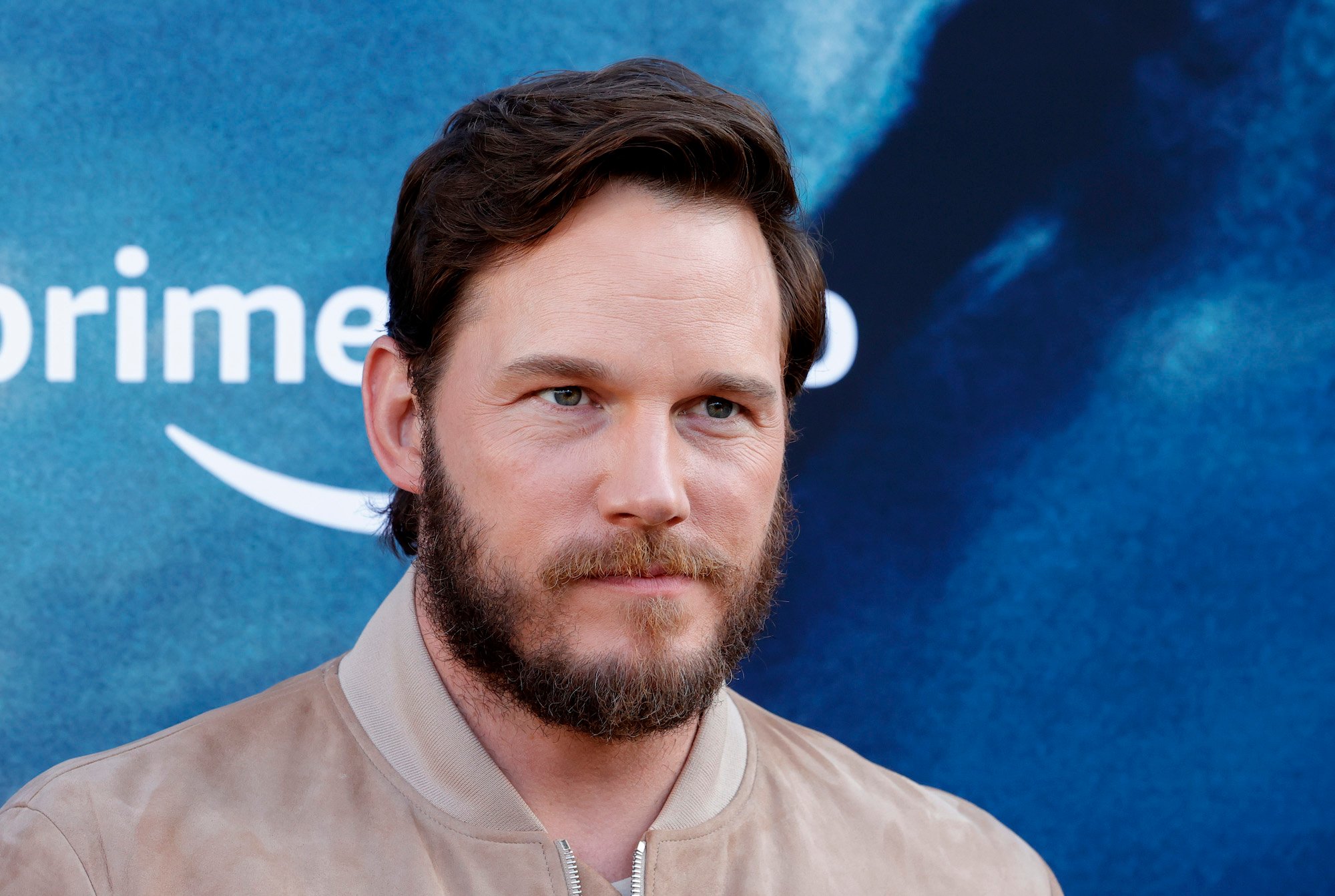 Chris Pratt wearing a tan jacket in front of a blue background at the 'Tomorrow War' premiere