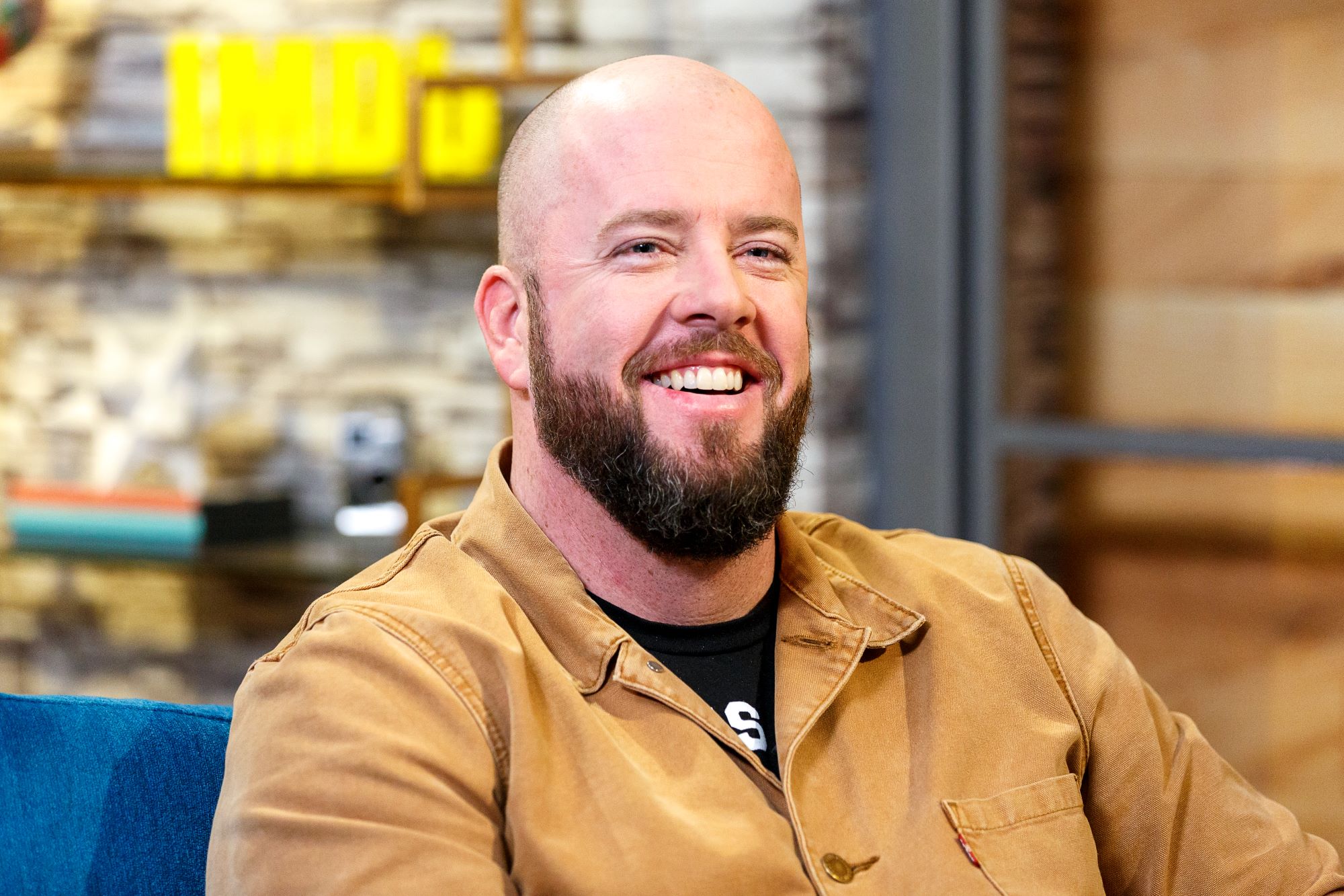 'This Is Us' Season 6 actor Chris Sullivan wears a tan button-up shirt over a black shirt.