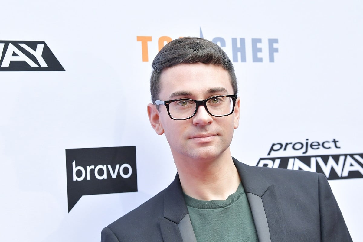 'Project Runway' Season 4 winner Christian Siriano in a black suit, green shirt, and black rimmed glasses posing for photographers on the red carpet.