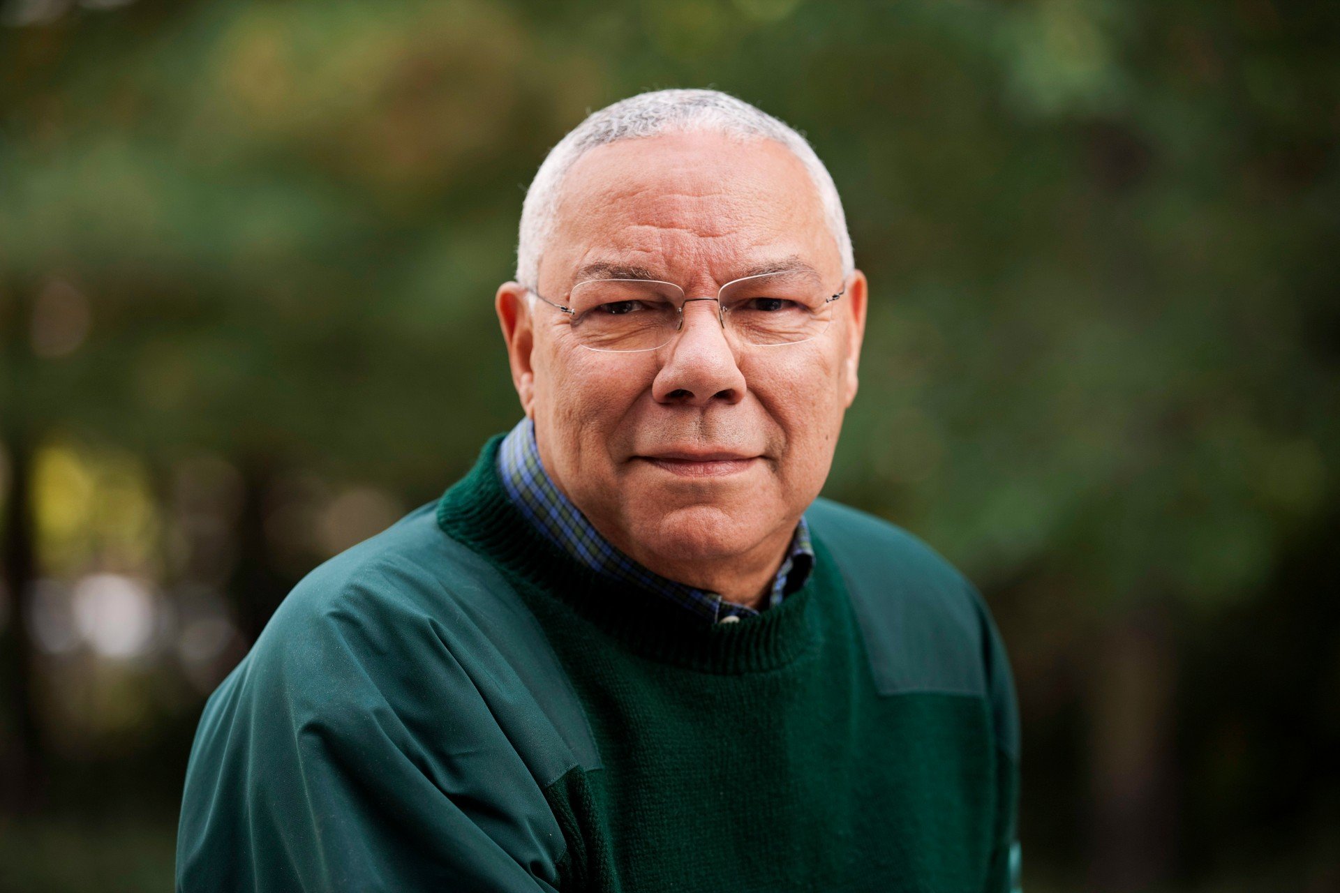 Colin Powell smiles while wearing a green shirt.