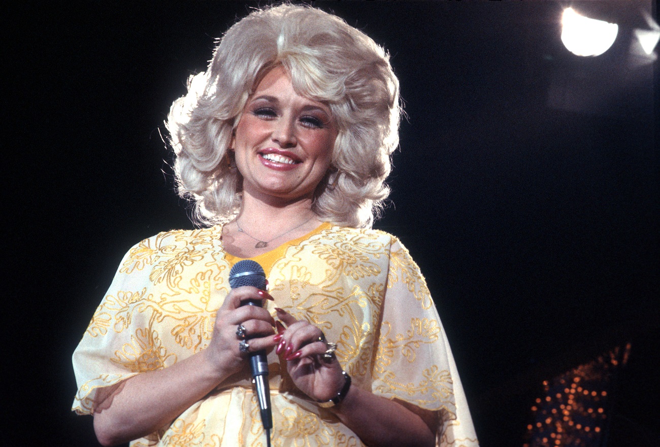 Dolly Parton wears a yellow dress and holds a microphone onstage.
