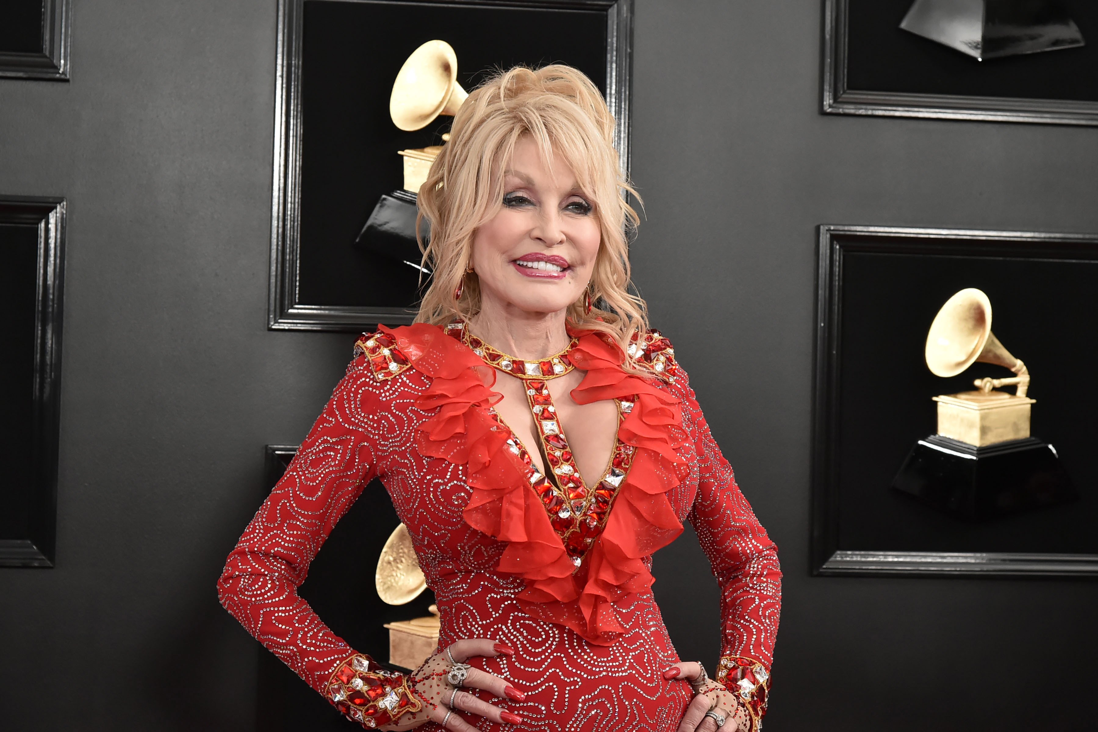 Dolly Parton smiles on the Grammy Awards red carpet in a red dress.