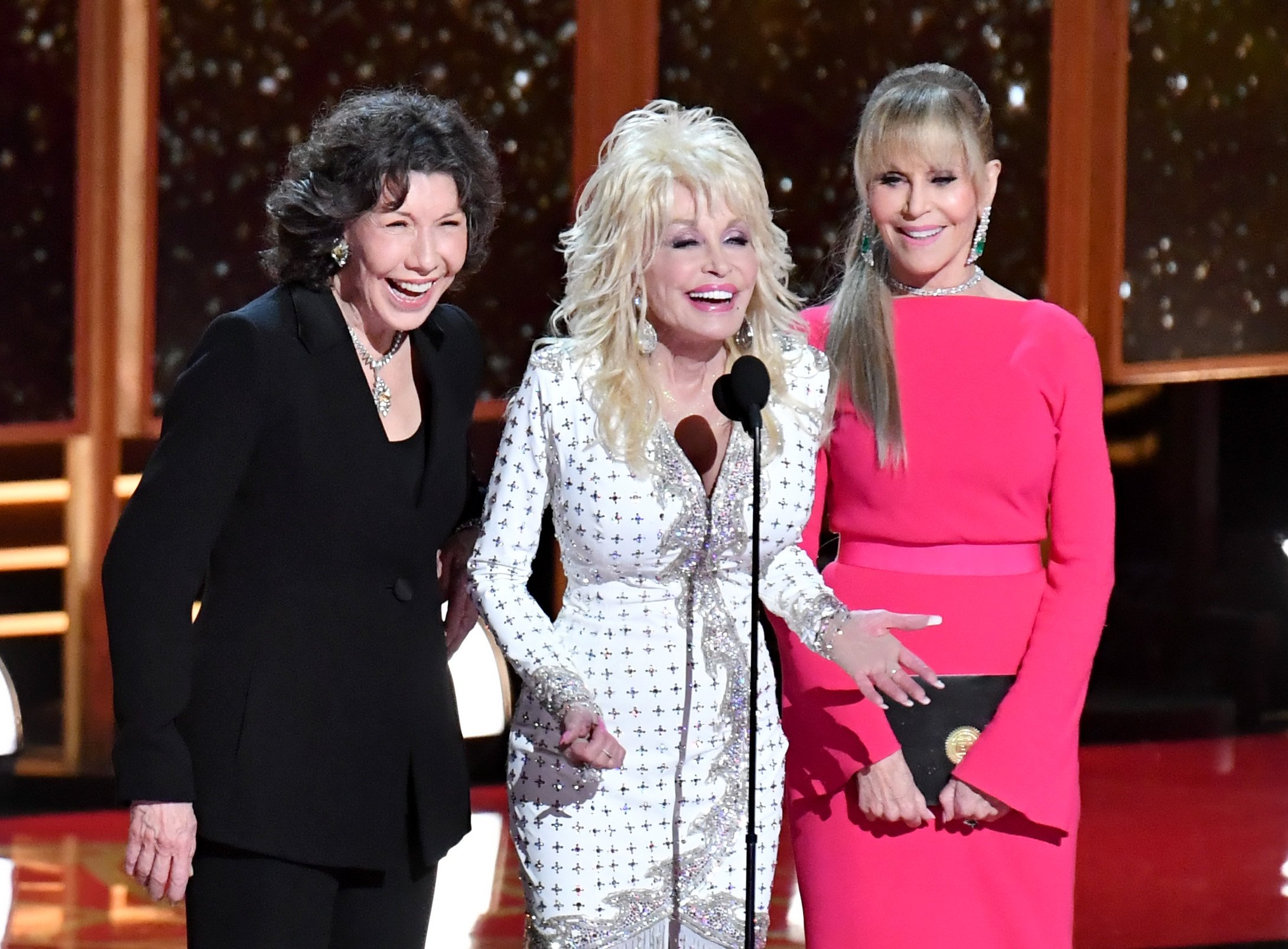 Grace and Frankie stars Jane Fonda and Lily Tomlin beside Dolly Parton speak onstage during the 69th annual Emmy Awards.