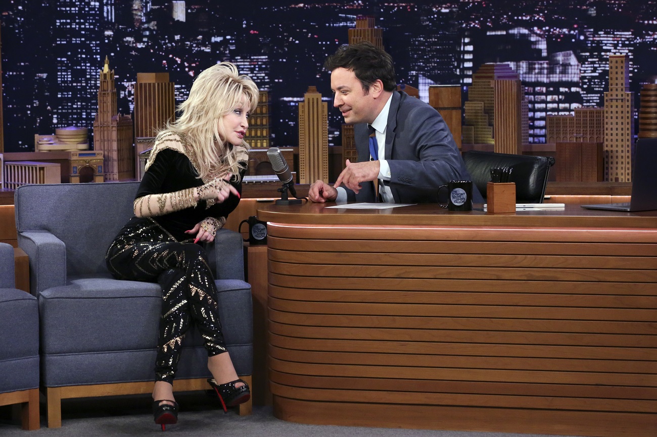 Dolly Parton in a black outfit and Jimmy Fallon in a suit talk to one another on 'The Tonight Show with Jimmy Fallon.