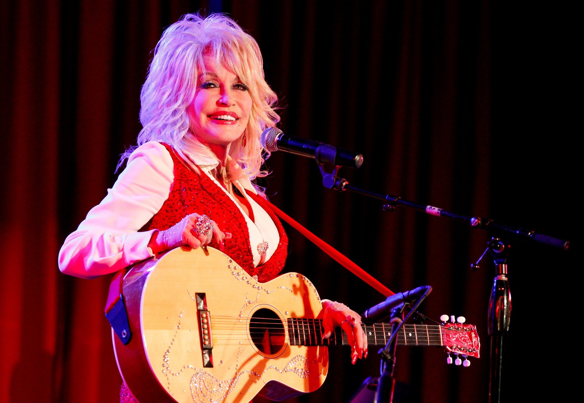 Dolly Parton smiles while holding her guitar
