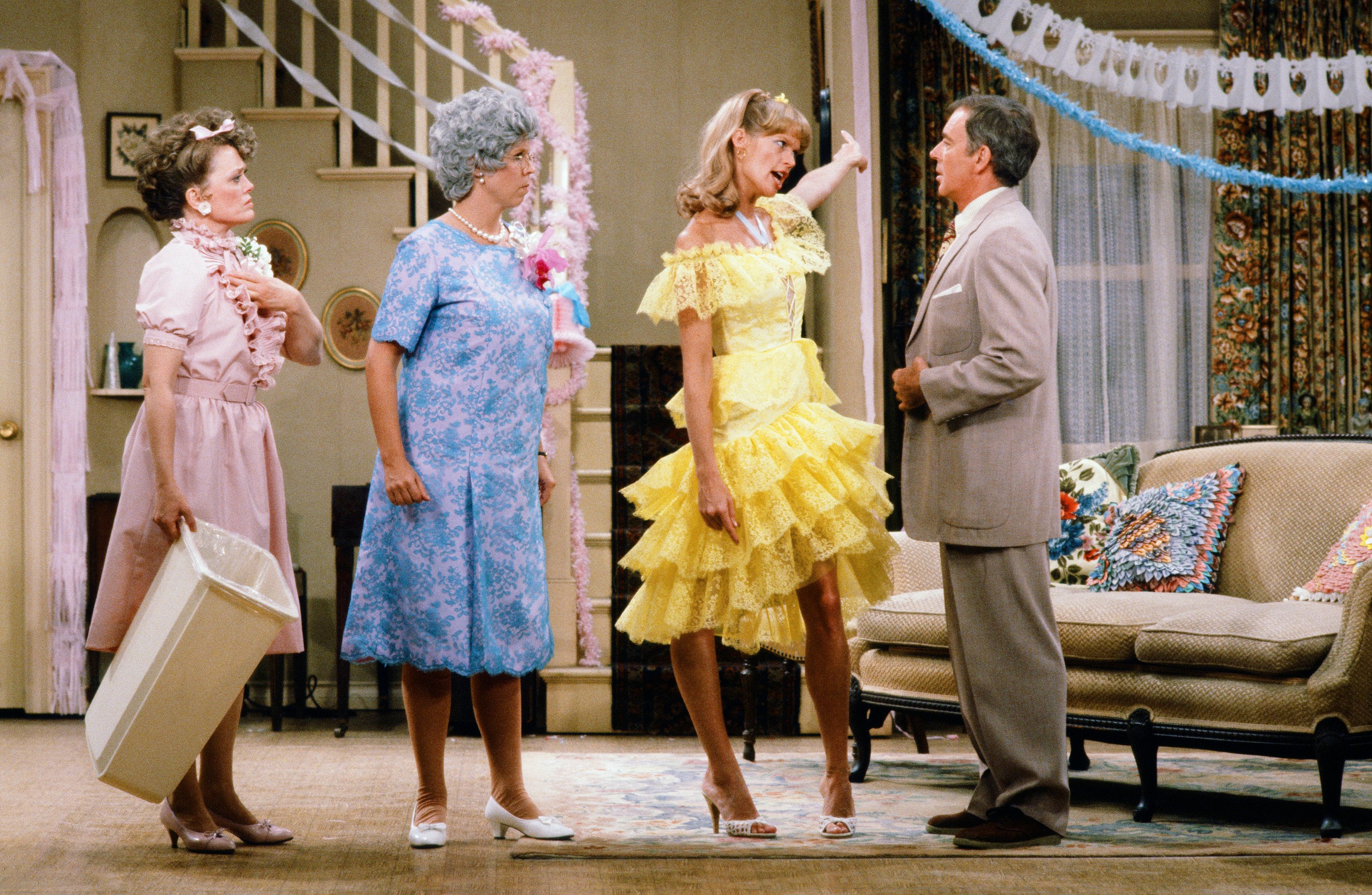 Rue McClanahan in a pink dress, Vicki Lawrence in a blue floral dress, Dorothy Lyman in a yellow dress, and Ken Berry in a tan suit film a scene for 'Mama's Family.'