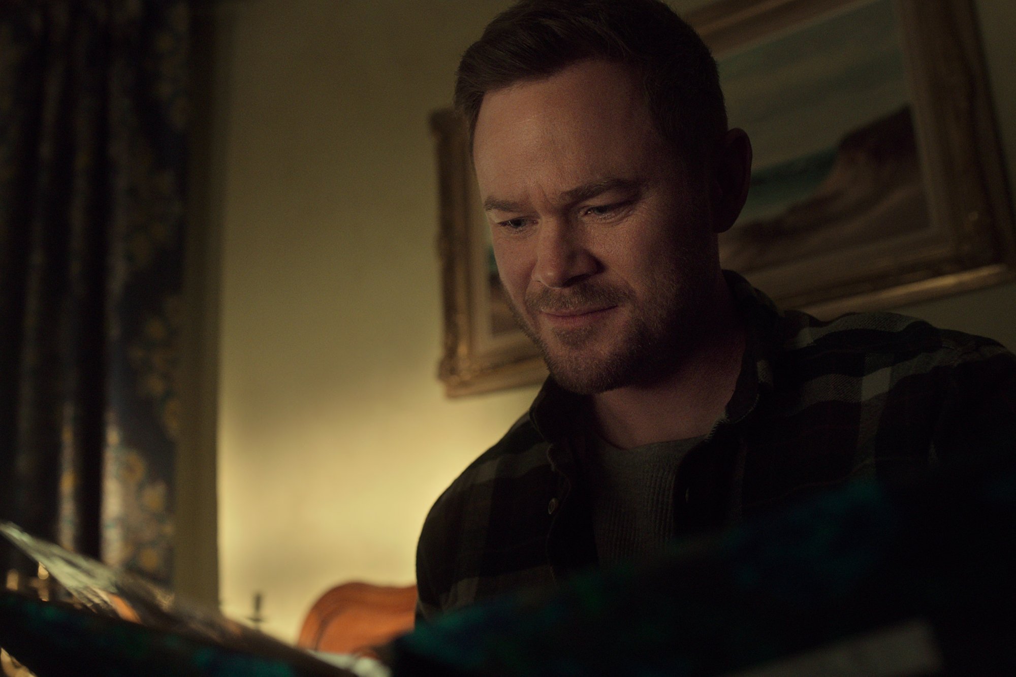 Aaron Ashmore as Duncan Locke in 'Locke & Key' Season 2 on Netflix. He's looking at a book and smiling.