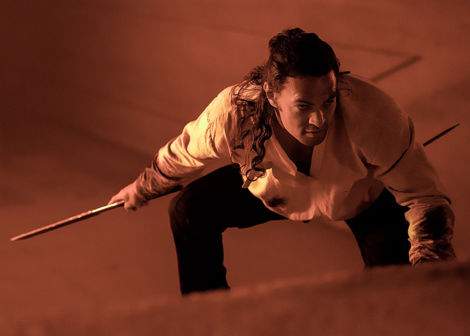 'Dune' star Jason Momoa wearing a white shirt and dark pants while holding a weapon