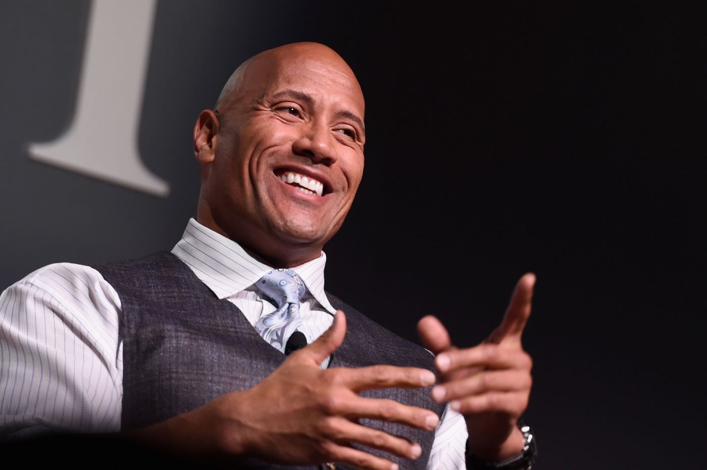 Dwayne Johnson in a white and grey pin stripped dress shirt with a grey vest.